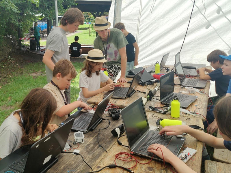 Kinder sitzen mit Laptops an einem Tisch in einem Pavillon