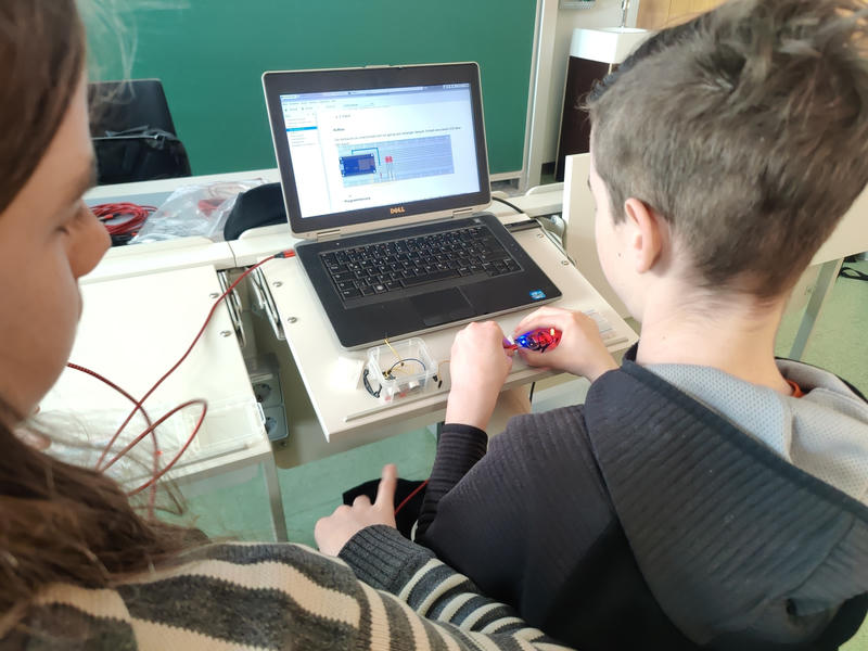 Blick über die Schulter von zwei Kindern, die eine LED auf einem Breadboard ausprobieren