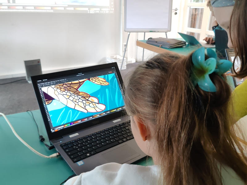 Ein Kind zeichnet an einem Laptop die Pfote eines Leoparden nach
