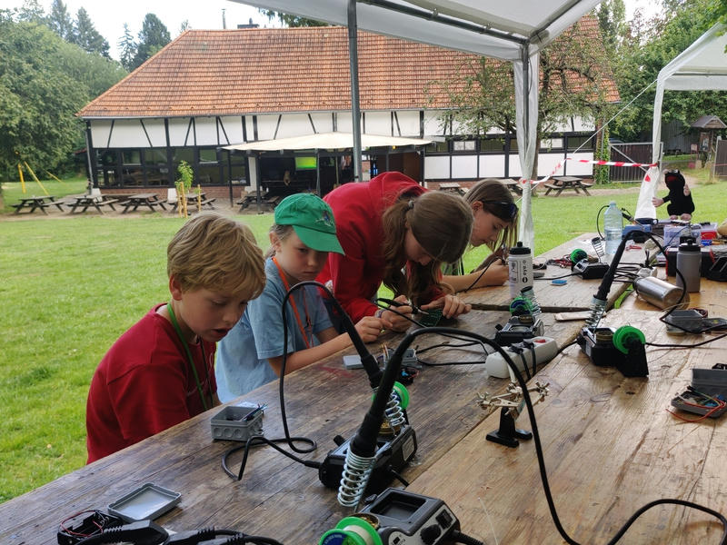 Kinder beim Elektronikbasteln in einem Pavillon auf einer großen Wiesen