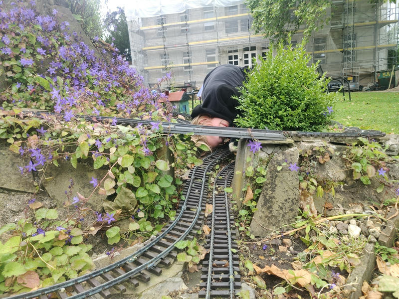 Ein Jugendlicher guckt unter einer Brücke einer Garten-Miniaturbahn hindurch.