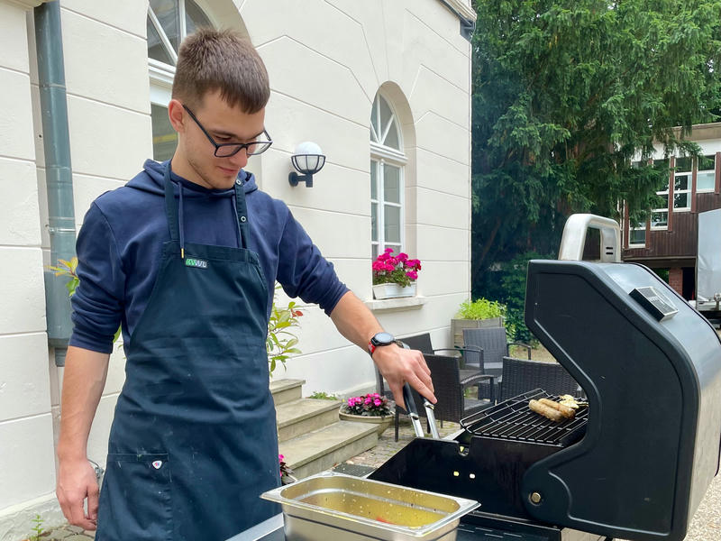 Tom steht vor dem Linuxhotel mit Schürze an einem Gasgrill.