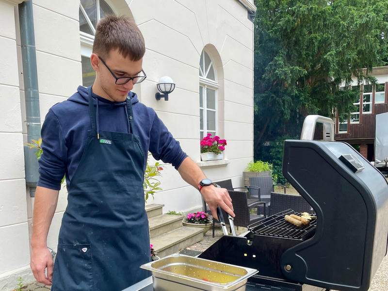 Tom steht vor dem Linuxhotel mit Schürze an einem Gasgrill.