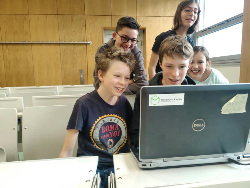 Mehrere Kinder lachen hinter einem Laptop, an dem sie ein Spiel ausprobieren