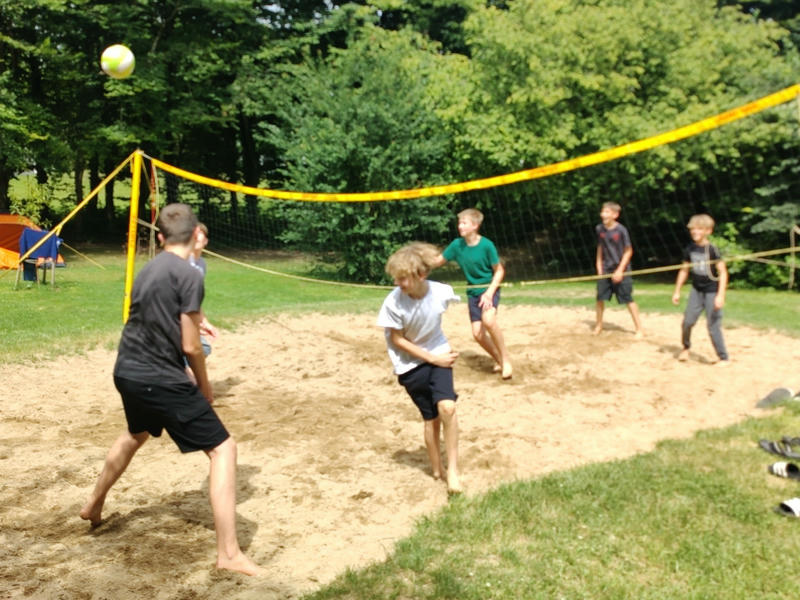 Kinder spielen Volleyball im Sand auf einer Wiese