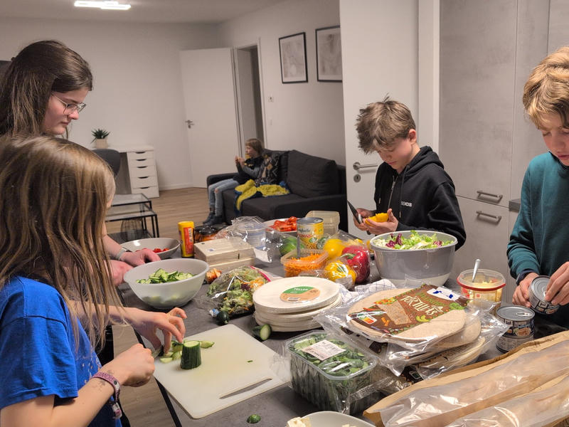 Kinder und Jugendliche stehen 
um einen Tisch bereiten Gemüse vor